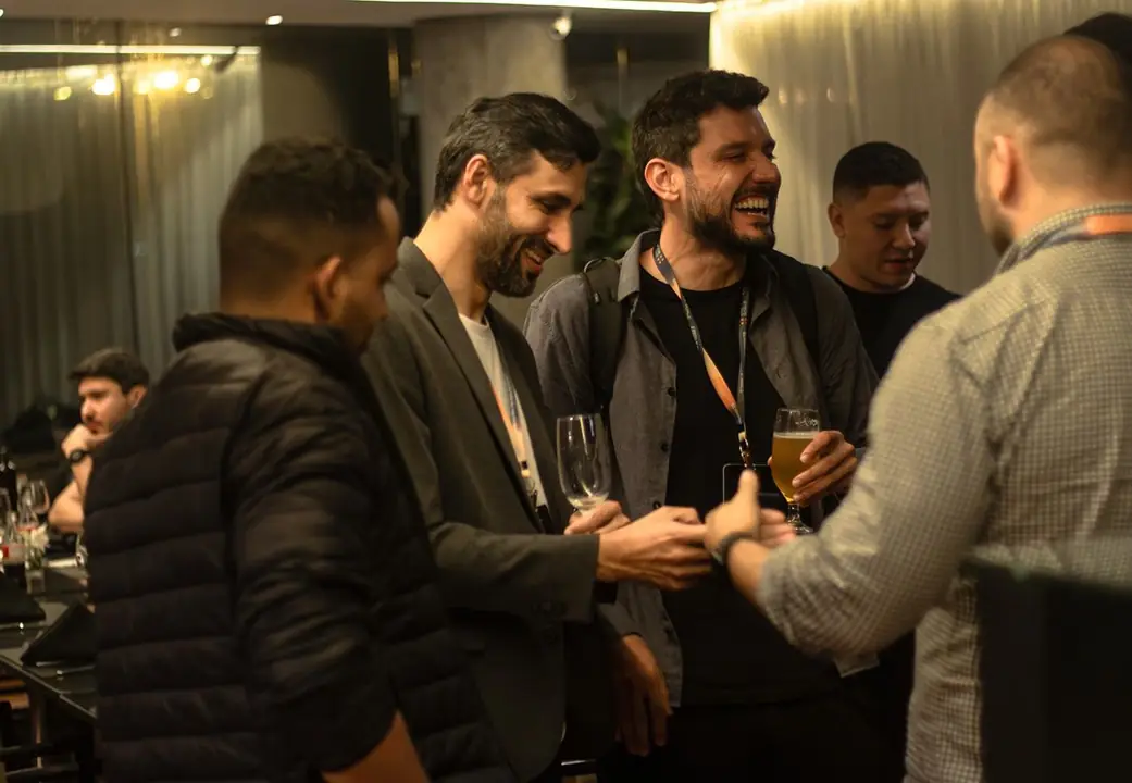 Participantes rindo e conversando em pé, com taças na mão