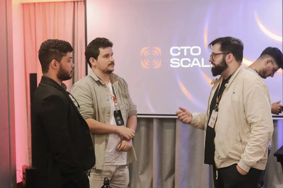 Três participantes conversando em frente ao telão da CTO Scale
